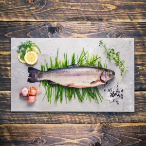 A whole rainbow trout on a board with herbs and assorted accompaniments